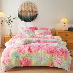 a bed with pink, yellow and green comforter in a room next to a lamp