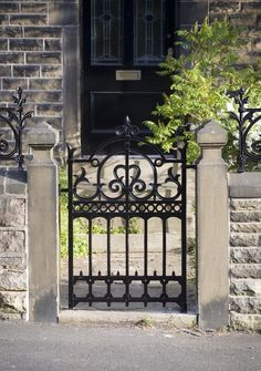 a black iron gate is in front of a brick building with a tree growing out of it