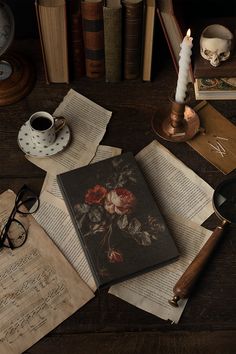 an open book sitting on top of a wooden table next to glasses and a candle