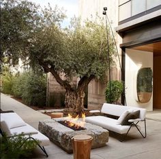 an outdoor living area with white furniture and a large tree in the middle of it