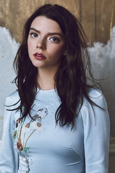 a woman with long dark hair wearing a blue shirt and standing in front of a wall