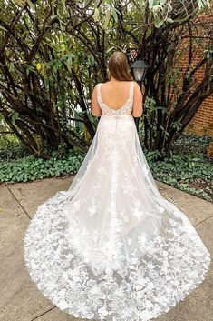 a woman in a wedding dress standing on the sidewalk with her back to the camera