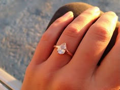 a woman's hand holding a ring with a pear shaped diamond on it,