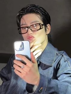 a man wearing glasses is looking at his cell phone while holding it up to his face