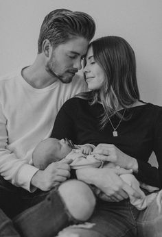 a man and woman holding a baby in their lap while looking at each other's eyes