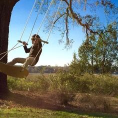 a man is swinging on a rope in the park while holding onto a tree branch