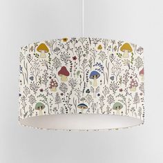 a lamp shade with mushrooms and plants on it hanging from a white ceiling light fixture