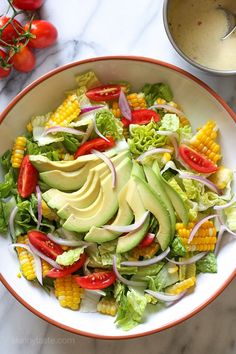 a salad with avocado, tomatoes and corn on the cob in a bowl