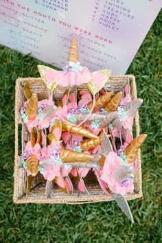 a basket filled with lots of pink and gold items on top of green grass next to a sign