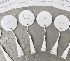 four white round tags with tassels are on a gray surface and the labels have writing on them