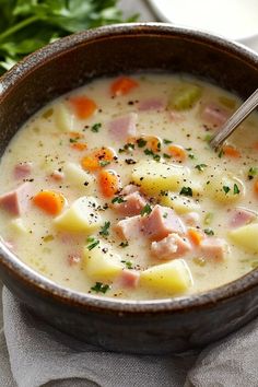 a bowl of ham and potato soup with a spoon in it on a napkin next to some parsley