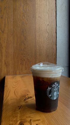 a cup of starbucks coffee sitting on top of a wooden table next to a wall