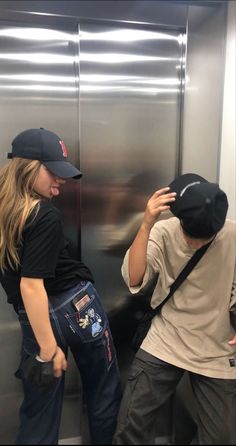 two people standing next to each other in front of a stainless steel wall and door