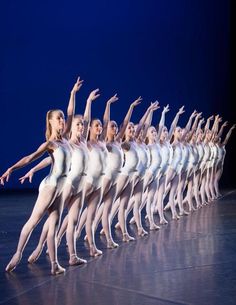 a line of ballet dancers in white outfits on stage with their arms up and hands out