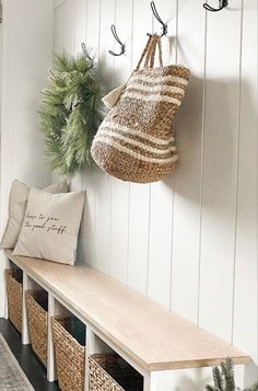 a bench with baskets on it next to a coat rack and potted plant in the corner