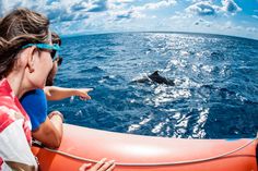 a woman points at a whale in the ocean while on a boat with another person