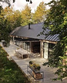 a wooden deck with tables and chairs on it next to some trees in the background