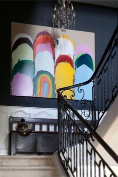 a staircase with art on the wall and chandelier hanging from it's handrail