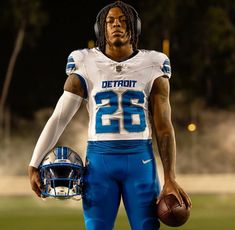 a football player with dreadlocks is holding a ball and wearing a detroit blue uniform