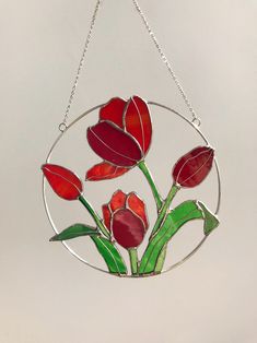 a stained glass sun catcher with red tulips in the center on a chain