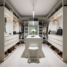 an organized closet with shoes and bags on the shelves, white stools in front of it