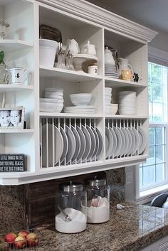 a kitchen with white cabinets and dishes on the shelves