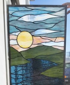 a hand holding up a stained glass window with the sun setting over a body of water