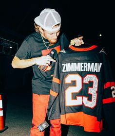 a man holding up a jersey with the number 23 on it while standing next to an orange cone