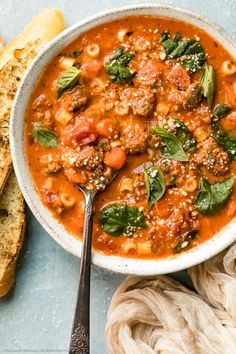 a white bowl filled with pasta and meat soup next to a baguette bread