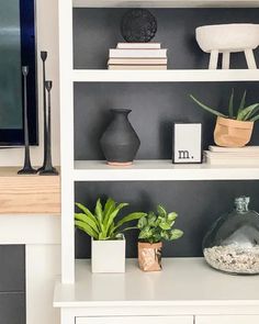 a white bookcase with plants and books on it in front of a flat screen tv