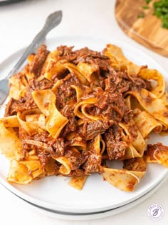 a white plate topped with pasta covered in meat and sauce next to a knife and fork