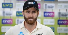 a man with a beard wearing a white shirt and black hat standing in front of a wall