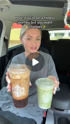 a woman sitting in the back seat of a car holding two cups of starbucks coffee