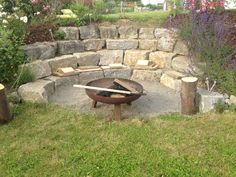 an outdoor fire pit surrounded by stone walls and trees with flowers in the back ground