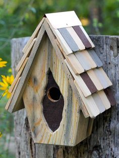 a birdhouse made out of wood on top of a tree stump with yellow flowers in the background