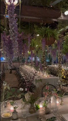 the tables are set up for an event with purple flowers and greenery hanging from the ceiling