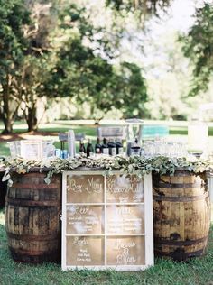 a wooden barrel filled with wine glasses and bottles on top of grass next to a sign