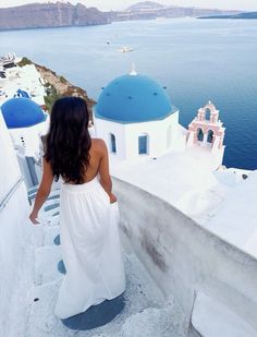 a woman in a white dress is walking up the stairs to a blue domed building