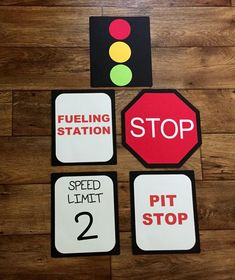 four different signs on a wooden floor with a stop light and fueling station sign