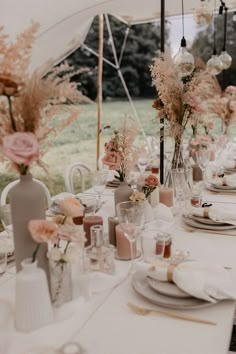 the table is set with white linens and pink flowers in vases on each side