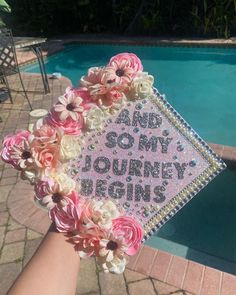 someone is holding up a pink and white graduation cap with flowers on it near a swimming pool