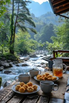 two plates of food on a wooden table next to a river with mountains in the background