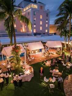 an outdoor event with tables and chairs set up in the grass at night, surrounded by palm trees