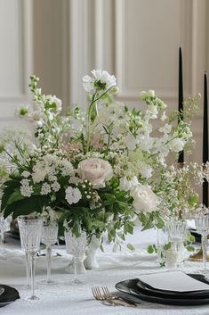 a centerpiece with white flowers and greenery sits on a table set for an elegant dinner