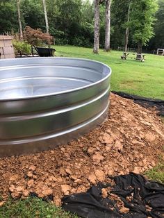 a large metal tub sitting on top of a dirt field next to a park bench