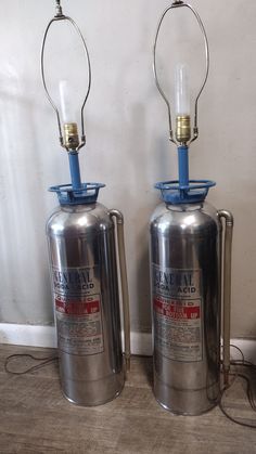 two large metal canisters sitting next to each other on the floor in front of a wall