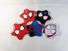 six spiderman shaped magnets sitting on top of a white sheet with black, red, and blue shapes