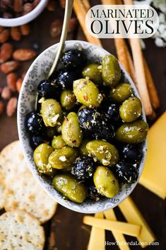 a bowl filled with olives next to crackers and cheese