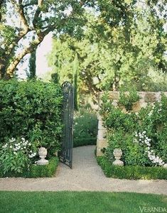 an open gate in the middle of a lush green garden with white flowers and greenery