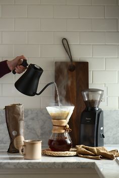 a person pouring coffee into a cup on top of a counter next to other items